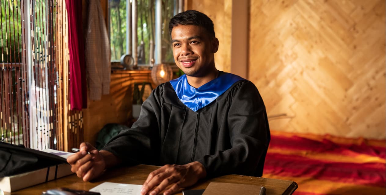 howsendSML An image of a man smiling, wearing a graduation robe